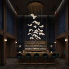 Folded shades from this Clérachic pendant light float above a dark bar with green stools, under a round gold ceiling plate.
