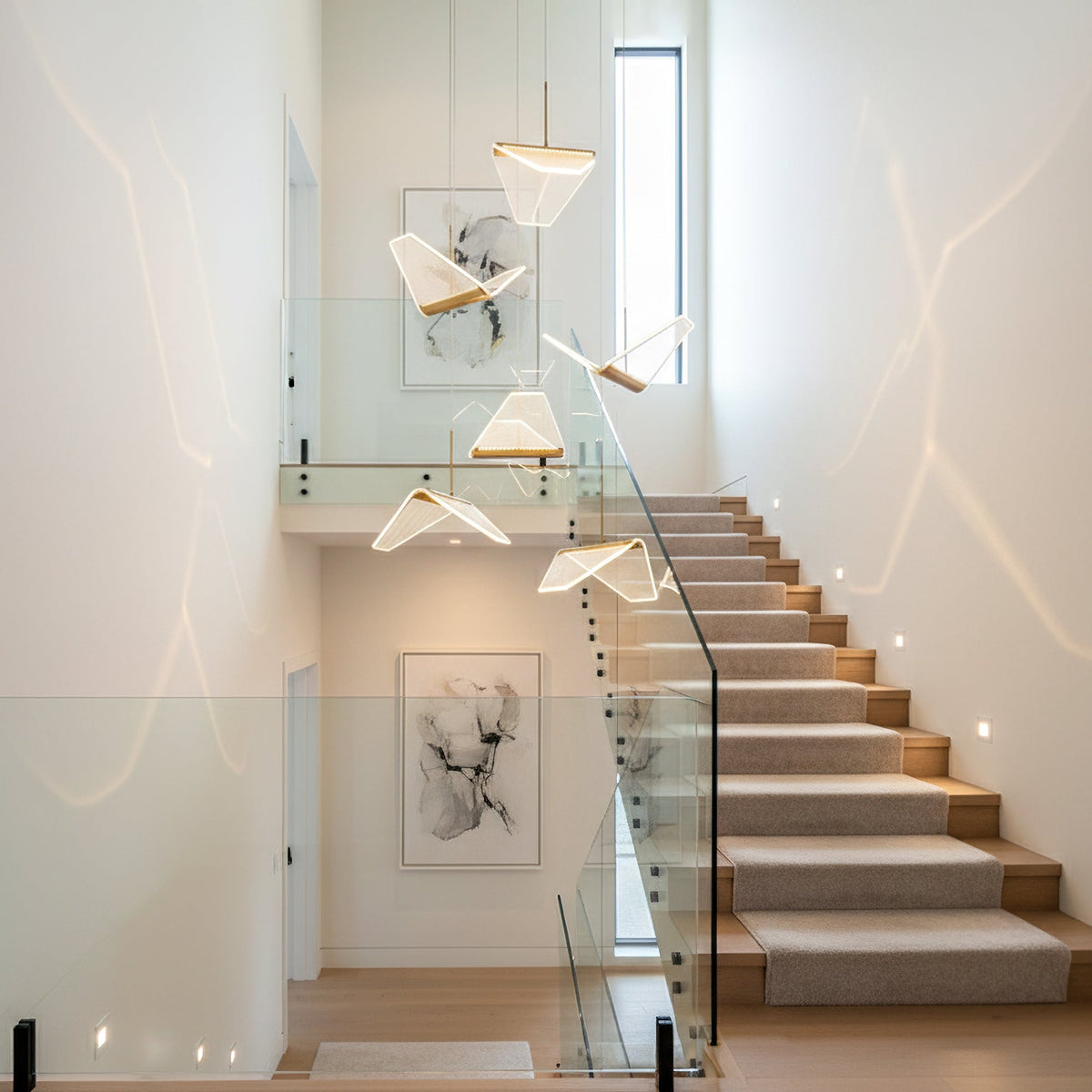 Several folded shades of this Clérachic pendant light hang in a stairwell beside a glass balustrade and framed artwork.