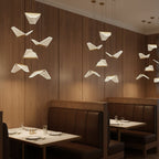 A group of folded shades from this Clérachic pendant light hangs against warm timber panelling above restaurant booths.