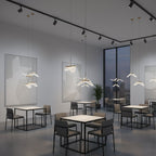 In a grey café space with track lighting and square tables, this Clérachic pendant light hangs folded shades at varied heights.