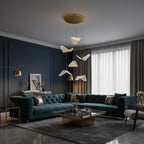 This Clérachic pendant light hangs folded shades above a teal Chesterfield sofa, with a dark blue wall behind.