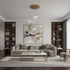 A Clérachic pendant light with a few folded shades hangs in a living room with a grey sofa, a brass-framed table and shelving.