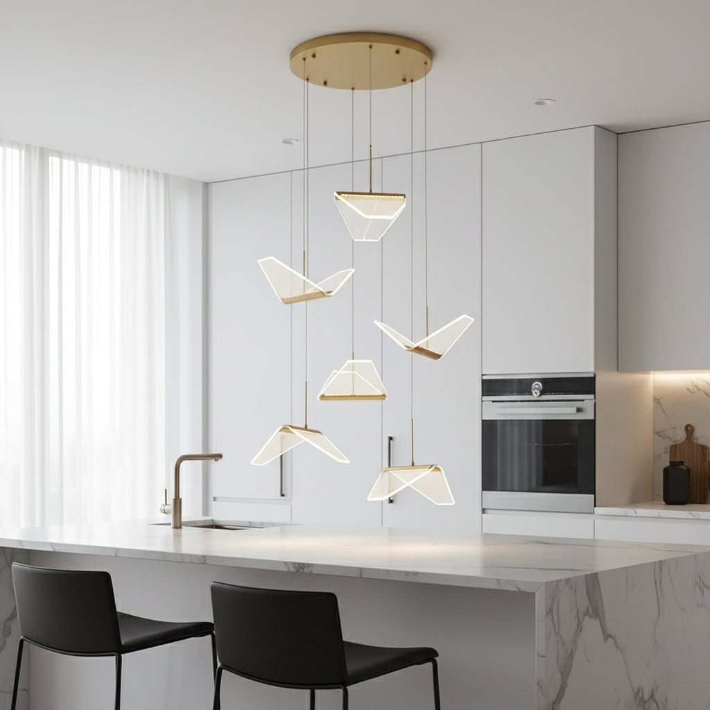 Folded shades from this Clérachic pendant light hang above a white marble island with black stools in a bright kitchen.