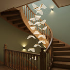 Folded shades of this Clérachic pendant light spiral down a curved wooden staircase against a sage-green wall.