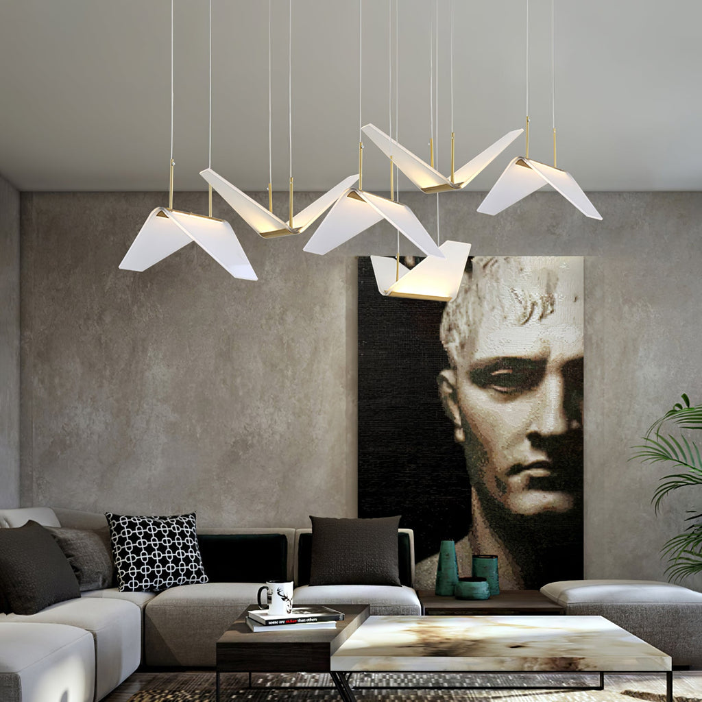 Folded white shades of this Clérachic pendant light hang over a grey sofa, with a large dark portrait on a textured wall.