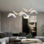 Folded white shades of this Clérachic pendant light hang over a grey sofa, with a large dark portrait on a textured wall.