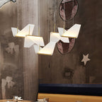 Close view of folded white shades from this Clérachic pendant light, each glowing along a gold underside, on a rough concrete wall.