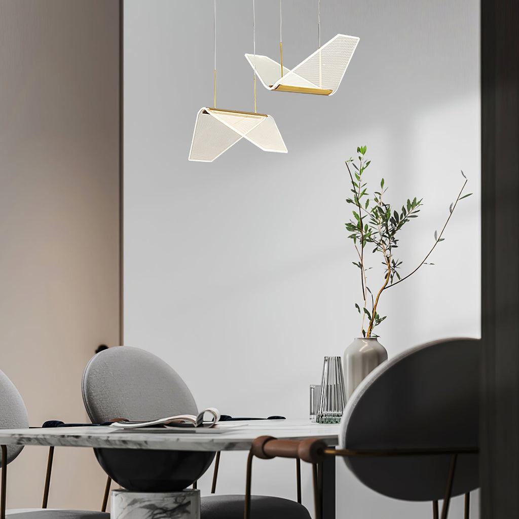 Two folded shades of this Clérachic pendant light hang above a round marble table with a vase of olive branches.