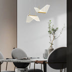 Two folded shades of this Clérachic pendant light hang above a round marble table with a vase of olive branches.