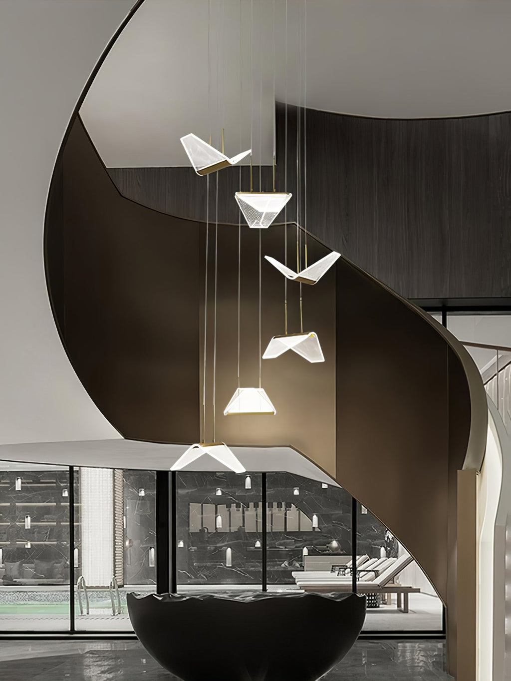 Folded shades from this Clérachic pendant light hang down the centre of a sweeping dark spiral staircase.