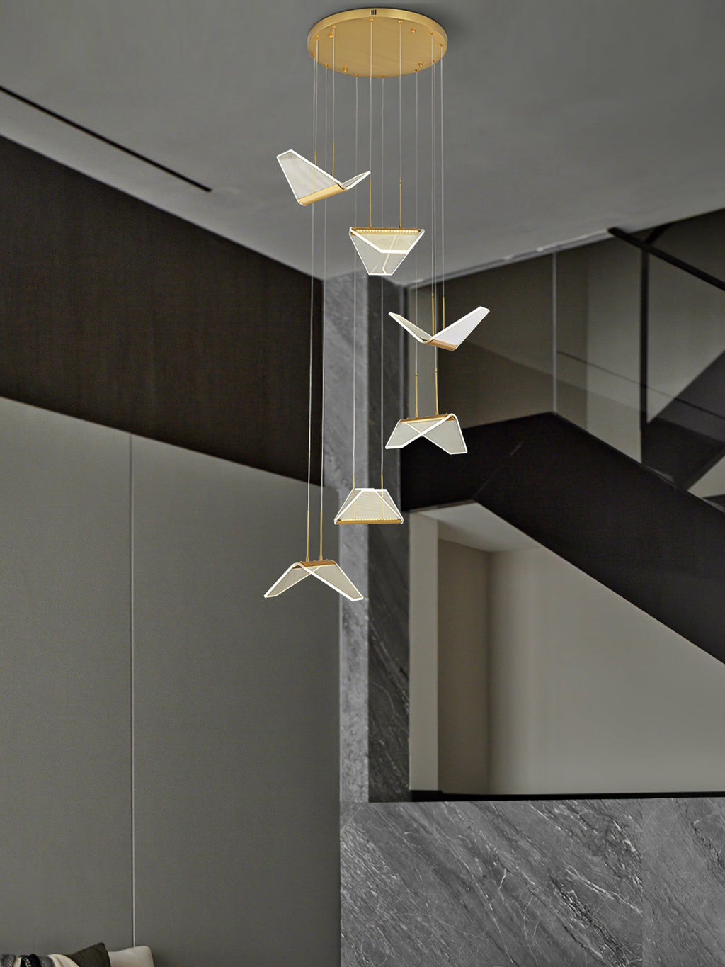 Pale folded shades of this Clérachic pendant light descend from a round gold plate beside a grey stone staircase.