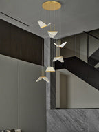 Pale folded shades of this Clérachic pendant light descend from a round gold plate beside a grey stone staircase.