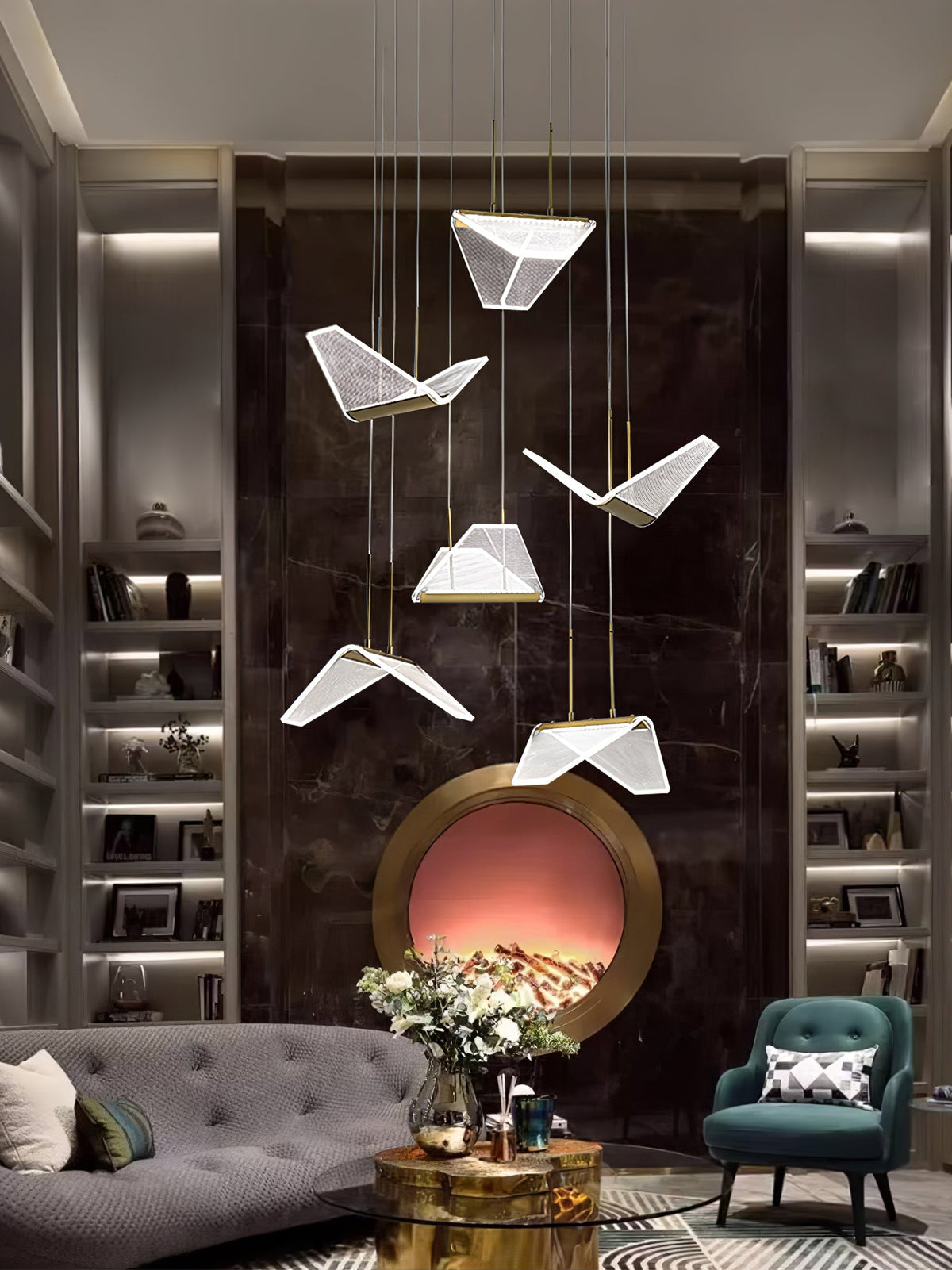 Folded clear shades of this Clérachic pendant light hang in front of a dark marble wall with shelving and a teal armchair.
