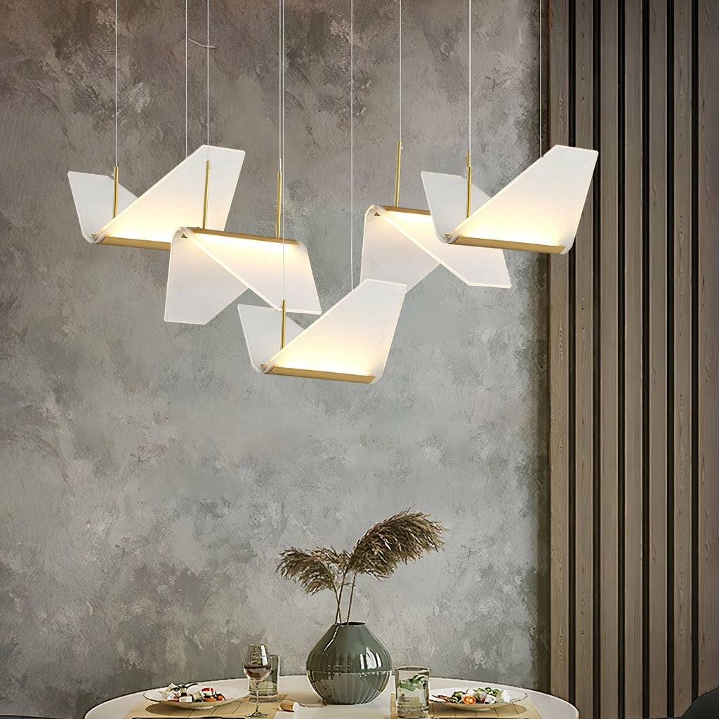 Folded white shades of this Clérachic pendant light glow along their gold edges against a grey plaster wall above a set table.