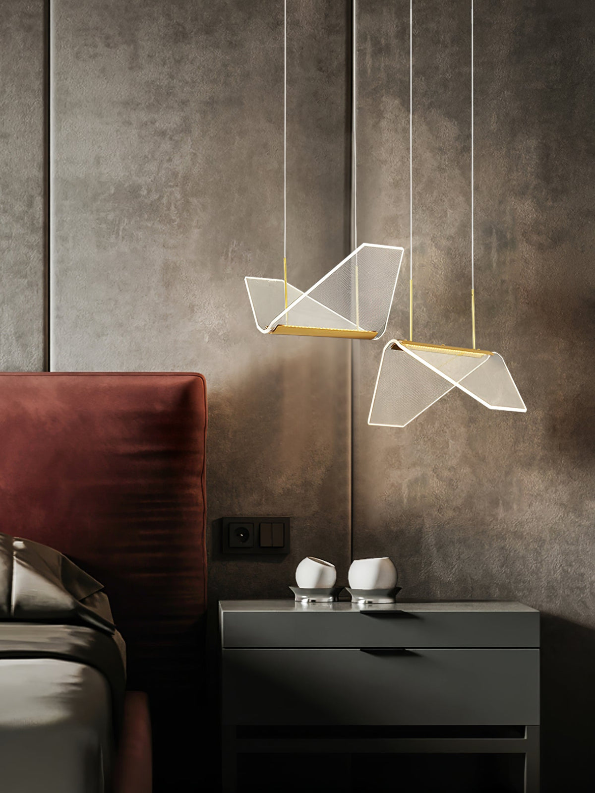 Two folded shades from this Clérachic pendant light hang beside a bed with a red headboard and a dark bedside cabinet.