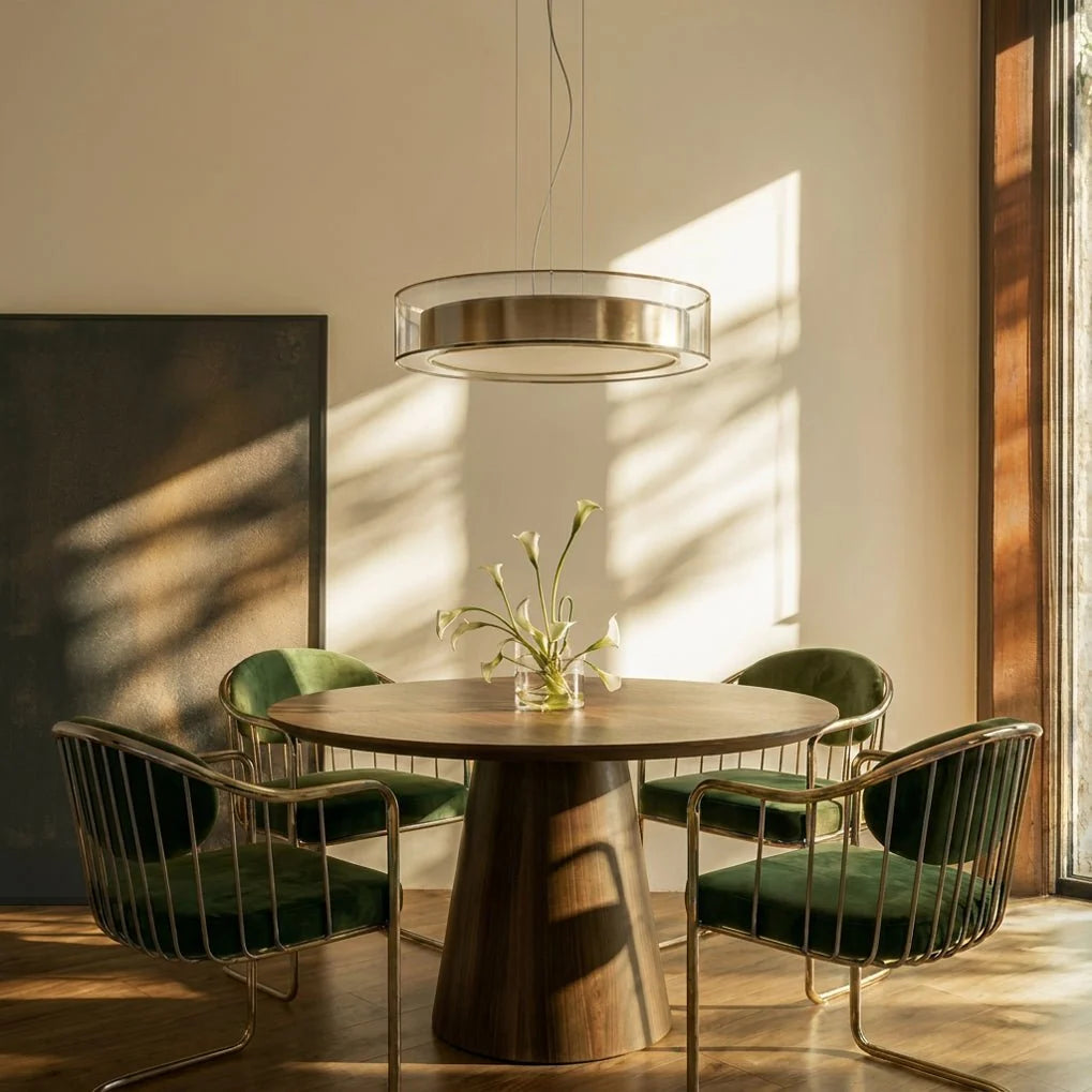 Clérachic's pendant light hanging above a round walnut dining table with green velvet chairs.