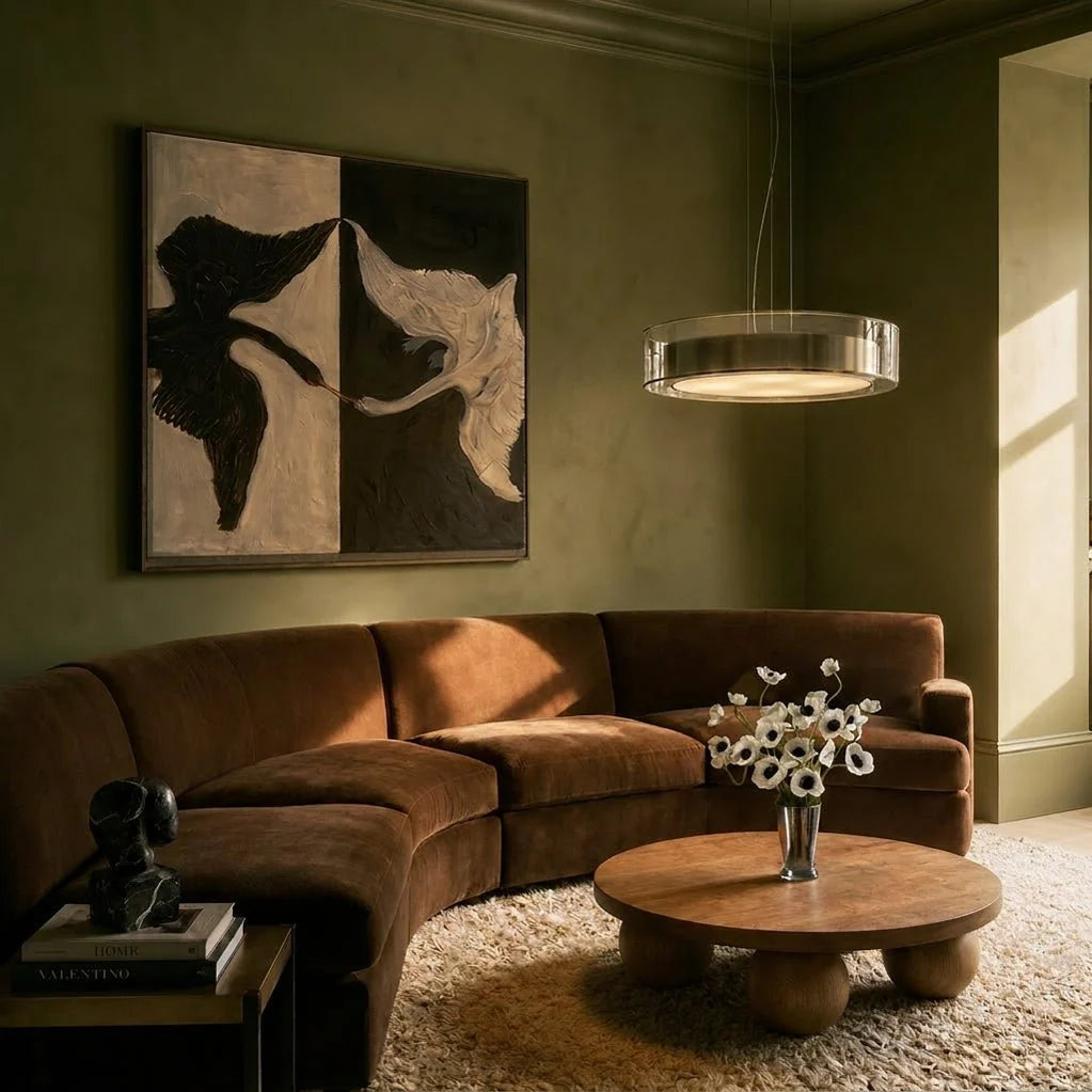 Clérachic's pendant light glowing warm in a moss-green living room beside a curved velvet sofa.