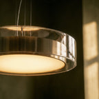 A close detail of the Clérachic pendant light's frosted diffuser glowing warm in a dim, moody room.