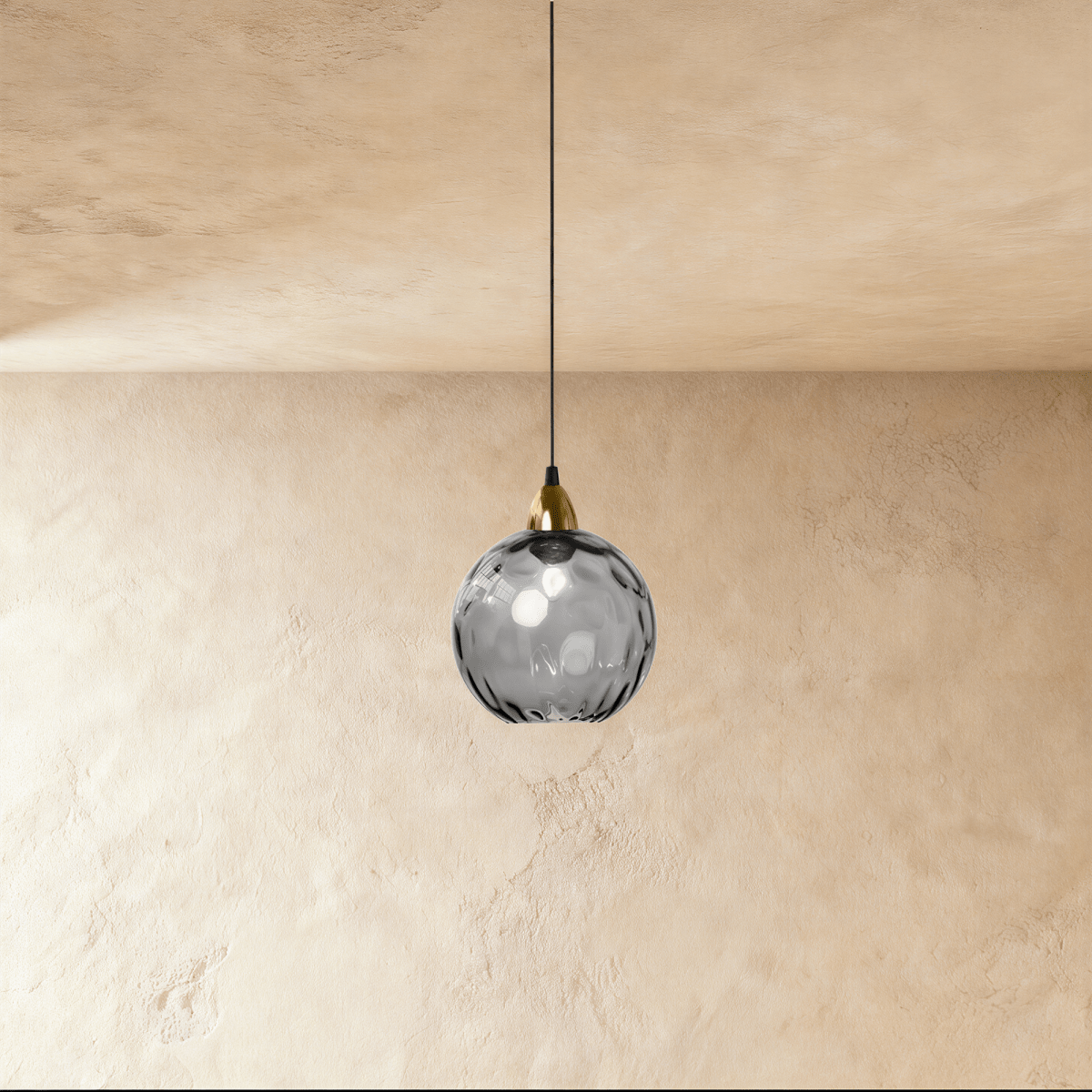 Clérachic gold pendant light with a smoky gray blown glass globe, hung from a brass fitting against a plaster wall.