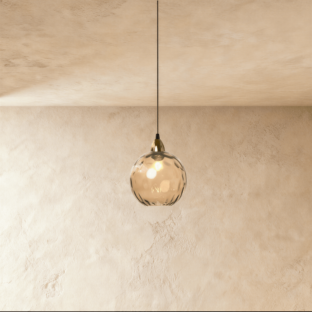 Clérachic gold pendant light with a cognac-toned blown glass globe, its dimpled texture catching warm light.