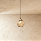 Clérachic gold pendant light with a cognac-toned blown glass globe, its dimpled texture catching warm light.
