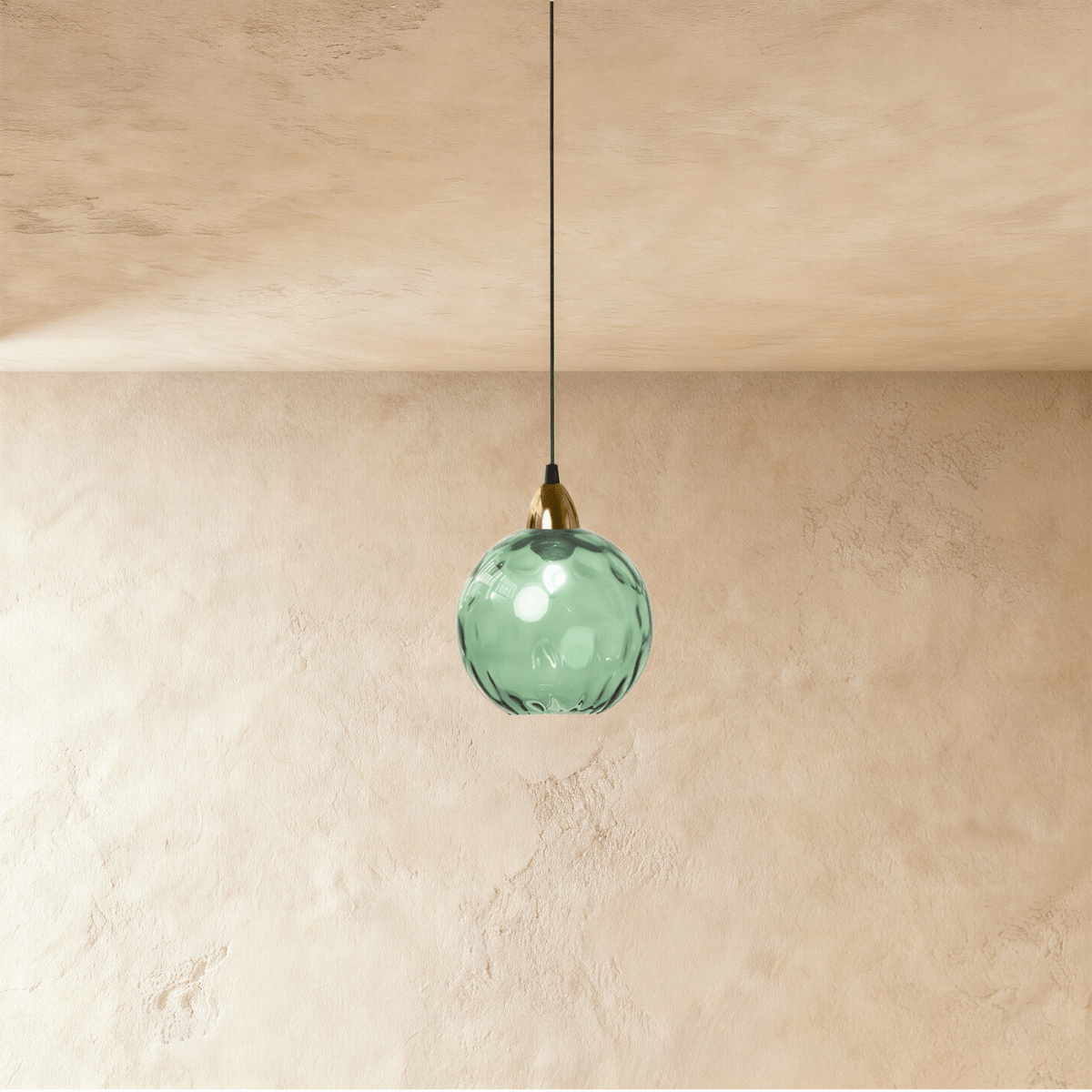 Clérachic gold pendant light with a green blown glass globe hanging from a brass cap against a plaster wall.