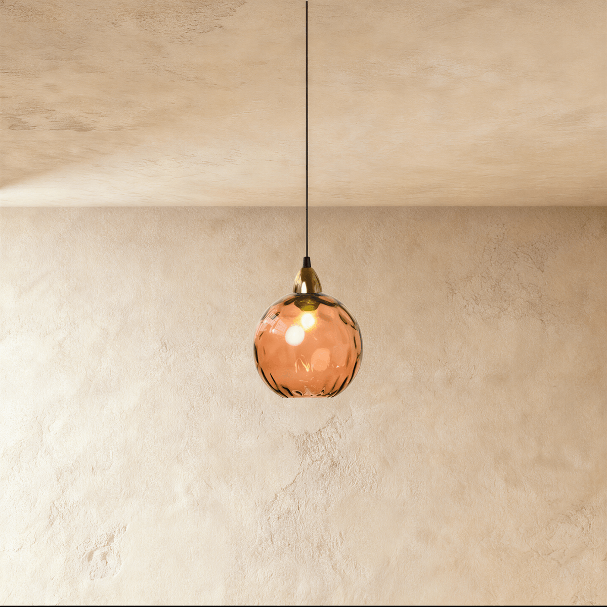 Clérachic gold pendant light with an orange blown glass globe, dimpled texture glowing warmly on a plaster wall.
