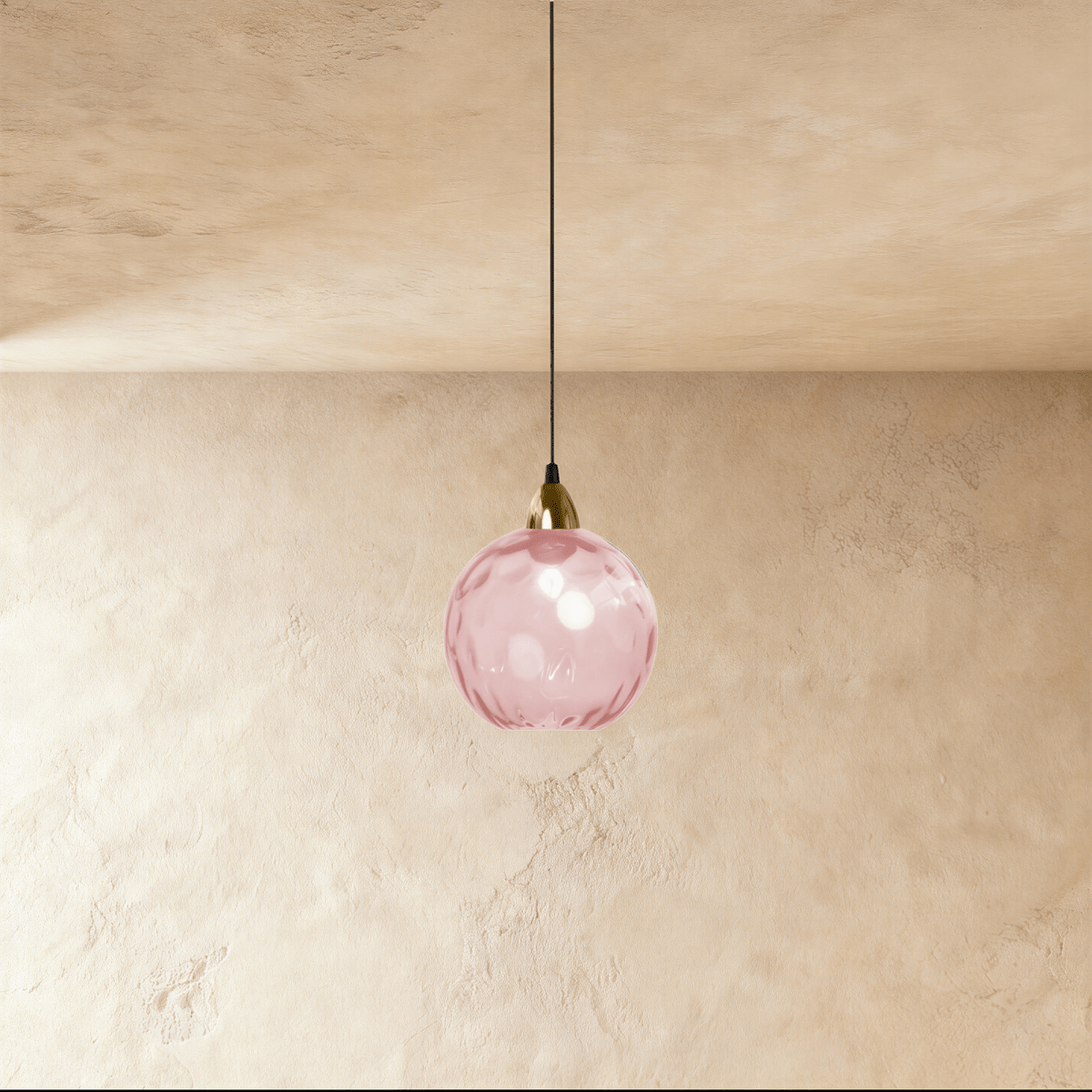 Clérachic gold pendant light with a pink blown glass globe suspended from a brass fitting on a plaster wall.