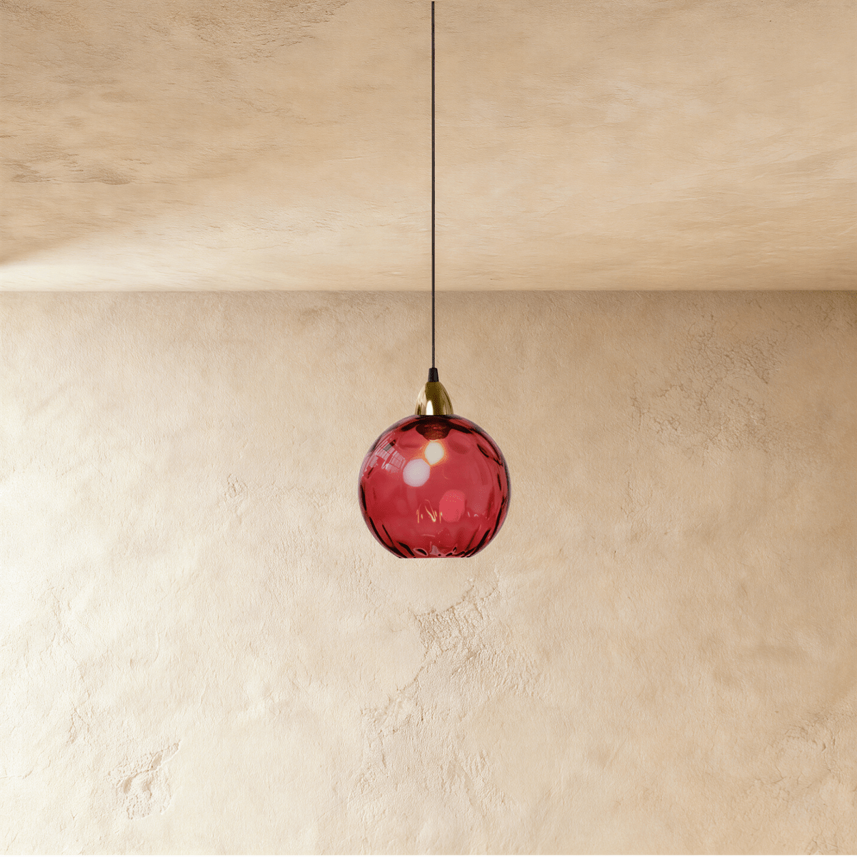 Clérachic gold pendant light with a red blown glass globe, its dimpled surface glowing above a plaster wall.