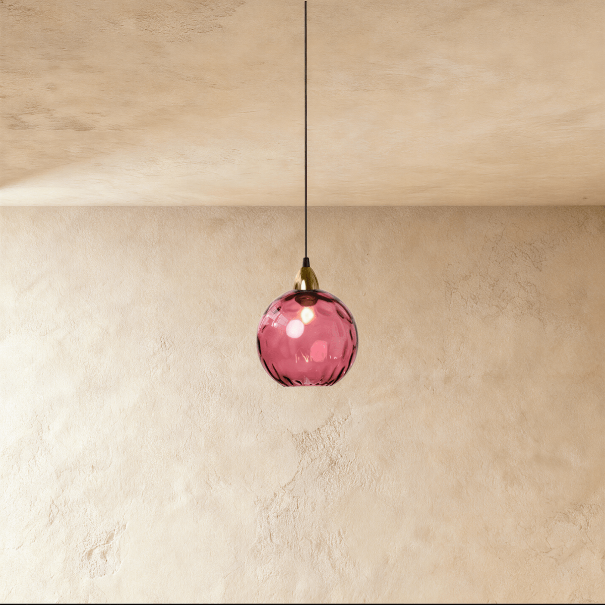 Clérachic gold pendant light with a rose red blown glass globe suspended from a brass cap on a plaster wall.