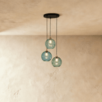 Clérachic gold pendant cluster with three blue and green blown glass globes hung at staggered heights from a black canopy.