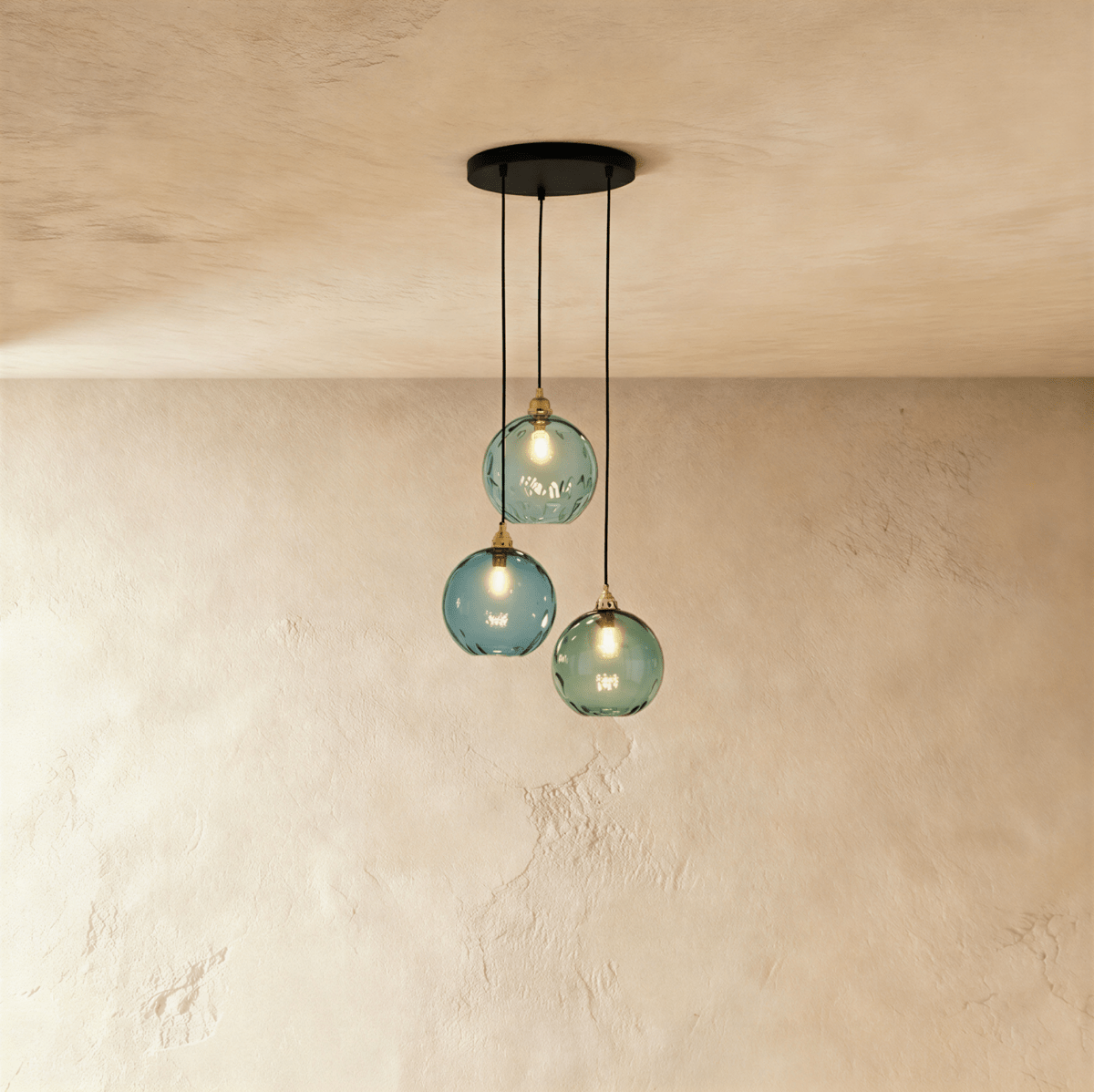 Clérachic gold pendant cluster with three blue and green blown glass globes hung at staggered heights from a black canopy.