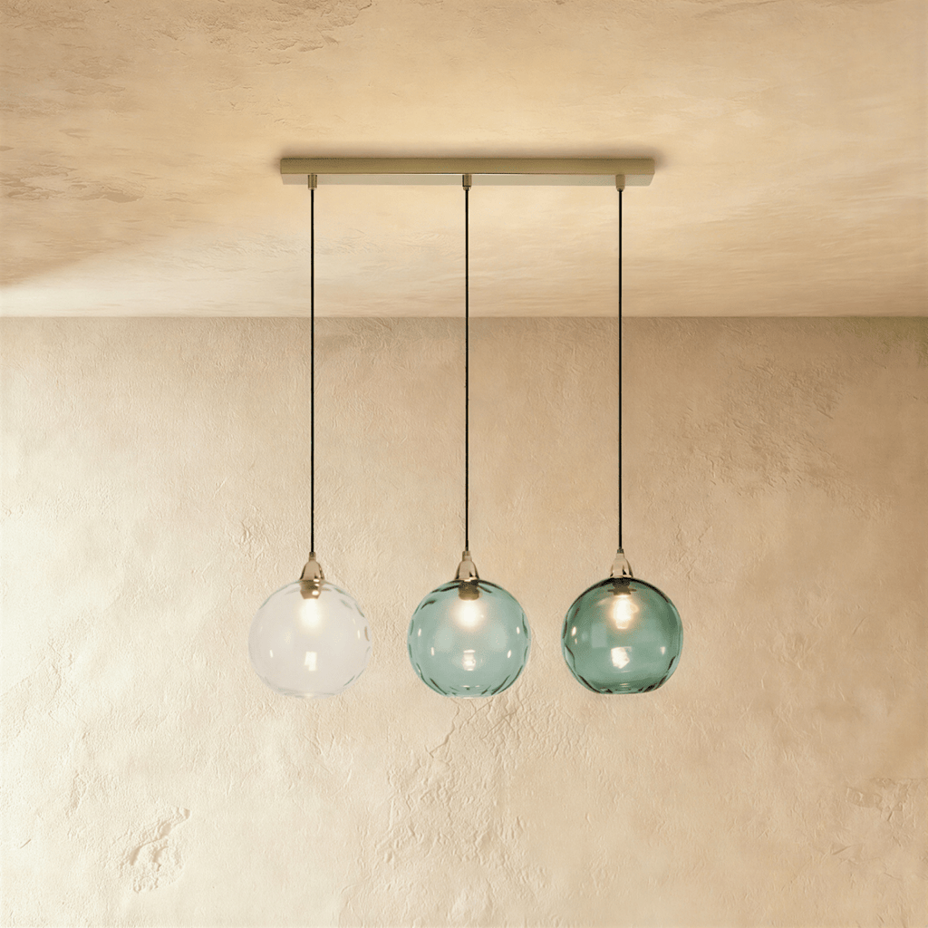 Clérachic gold pendant light with three blown glass globes in white and teal tones hung from a linear brass bar.
