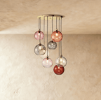 Clérachic gold pendant cluster with eight blown glass globes in mixed tones cascading from a round brass canopy.