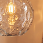 Close-up of a Clérachic pendant light's dimpled clear blown glass globe with the exposed filament bulb inside.