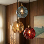 Close view of the Clérachic pendant cluster's blue, amber and red blown glass globes against a wood-paneled wall.
