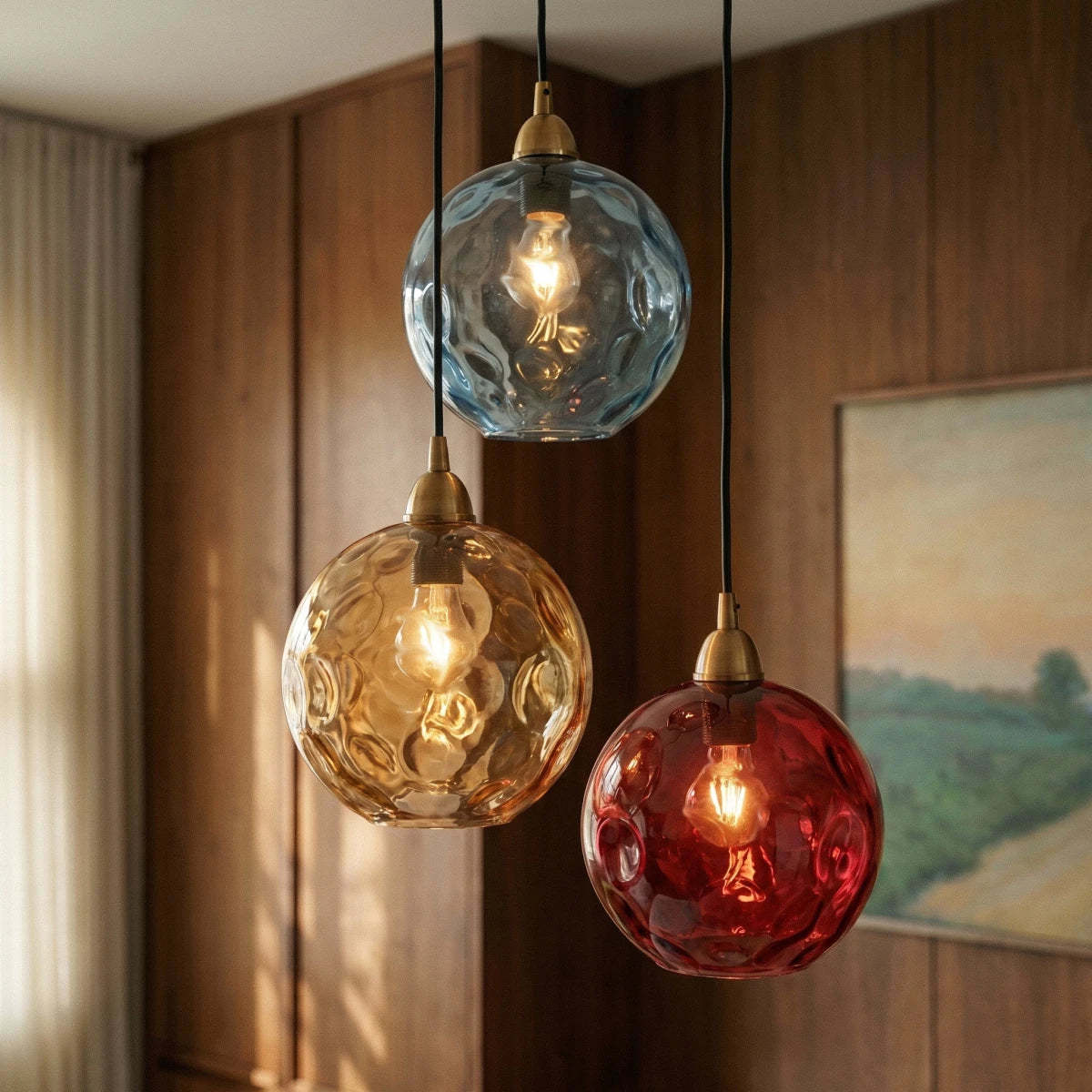 Close view of the Clérachic pendant cluster's blue, amber and red blown glass globes against a wood-paneled wall.