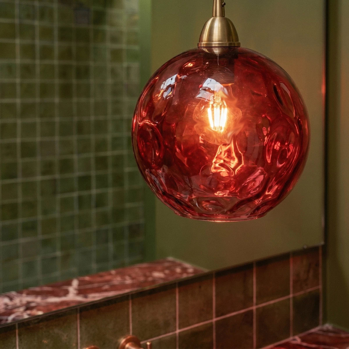 Close-up of the Clérachic pendant light's red blown glass globe, its dimpled texture glowing around the filament bulb.