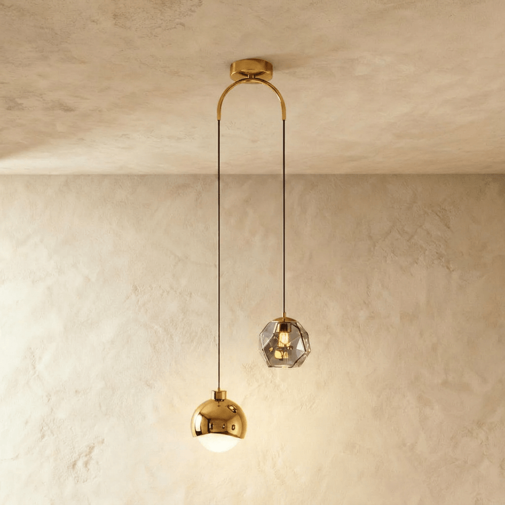 Clérachic pendant light in gold, a polished dome shade and a faceted glass gem hung at staggered heights.