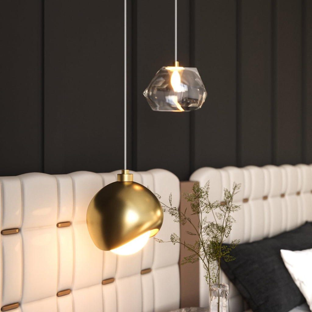 Clérachic pendant light in gold lit warm above a tufted white headboard in a dark panelled bedroom.