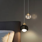 Clérachic pendant light in black lit warm beside a bed, its dome and faceted-glass shades against a dark wall.