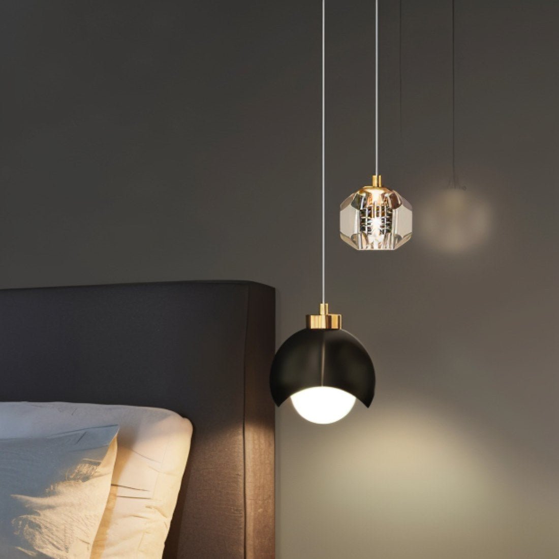 Clérachic pendant light in black lit warm beside a bed, its dome and faceted-glass shades against a dark wall.