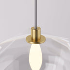 Clérachic pendant light detail, the brass socket and bulb glowing warm inside the faceted glass shade.