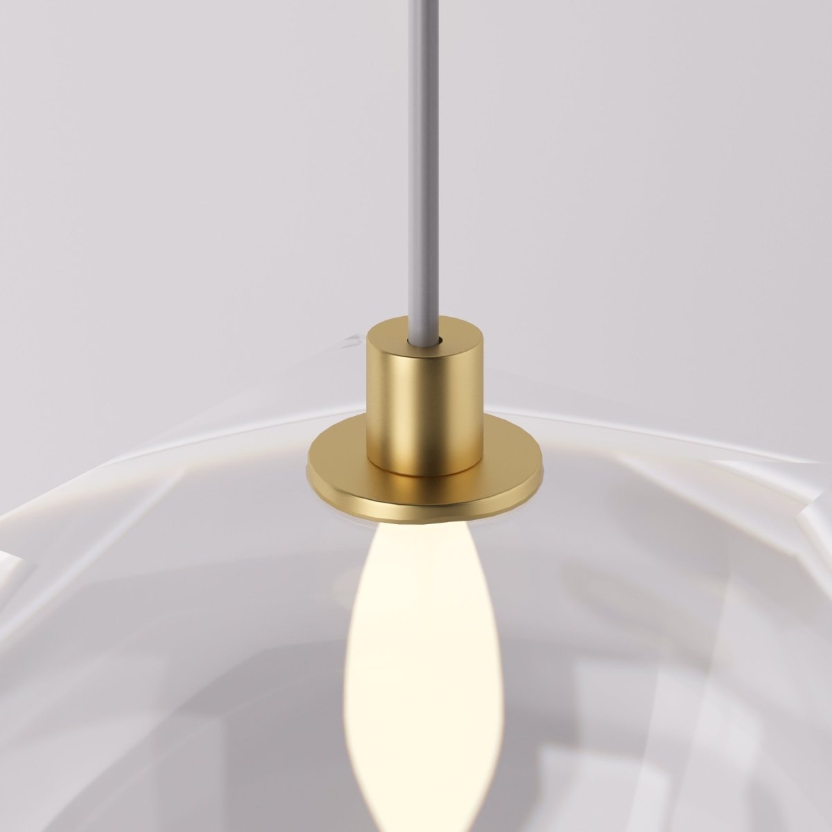 Clérachic pendant light detail, the brass socket and bulb glowing warm inside the faceted glass shade.