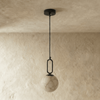 Clérachic pendant light with black metal fittings and a marbled alabaster globe, shown against a plaster wall.