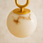Clérachic pendant light detail, gold oval hardware meeting a glowing alabaster globe with warm veining.