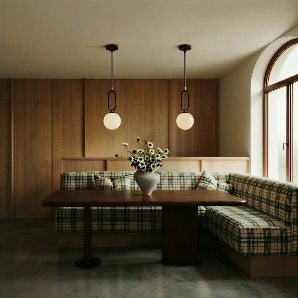 Clérachic black-hardware pendant lights, two hung above a plaid banquette in a wood-panelled dining nook.