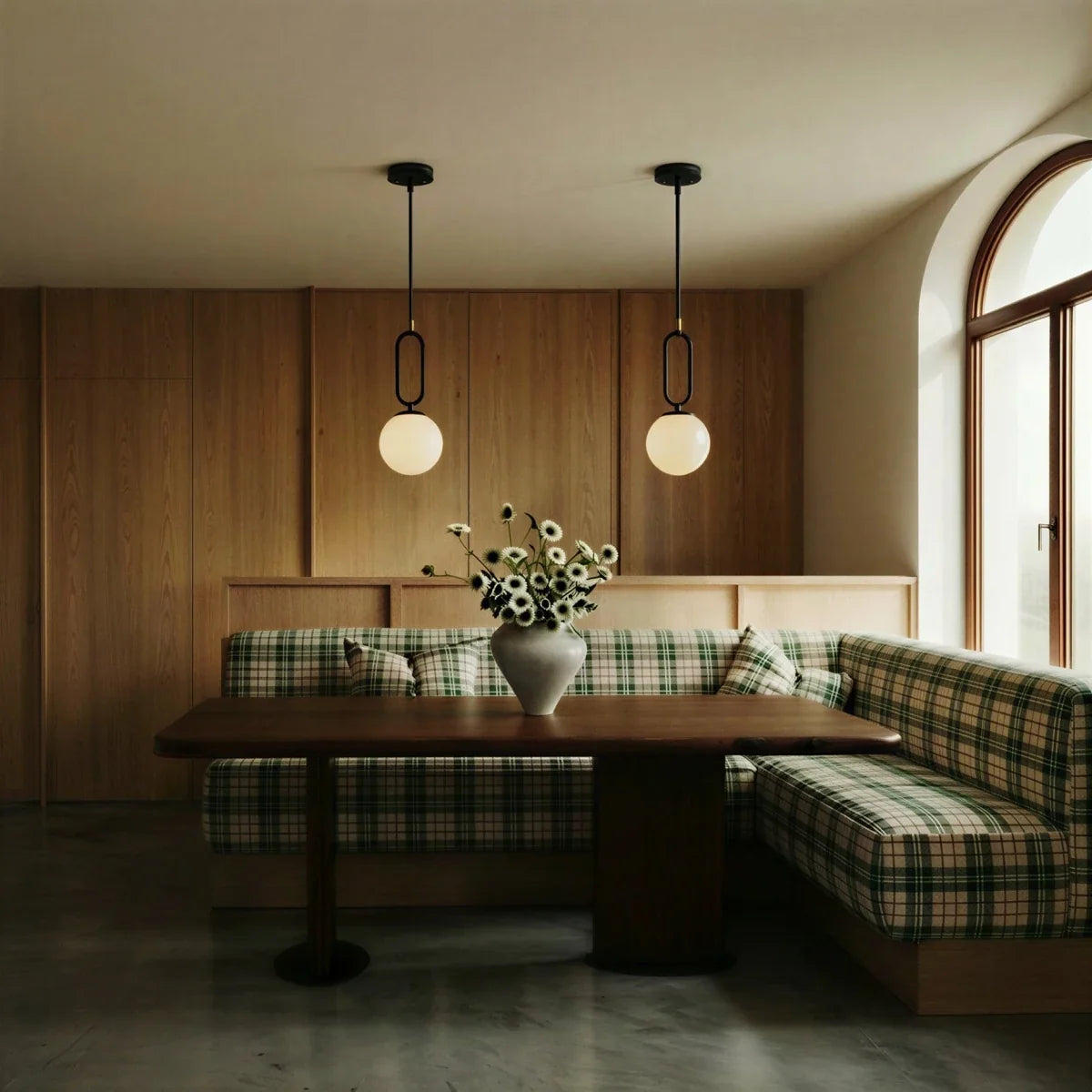 Clérachic black-hardware pendant lights, two hung above a plaid banquette in a wood-panelled dining nook.