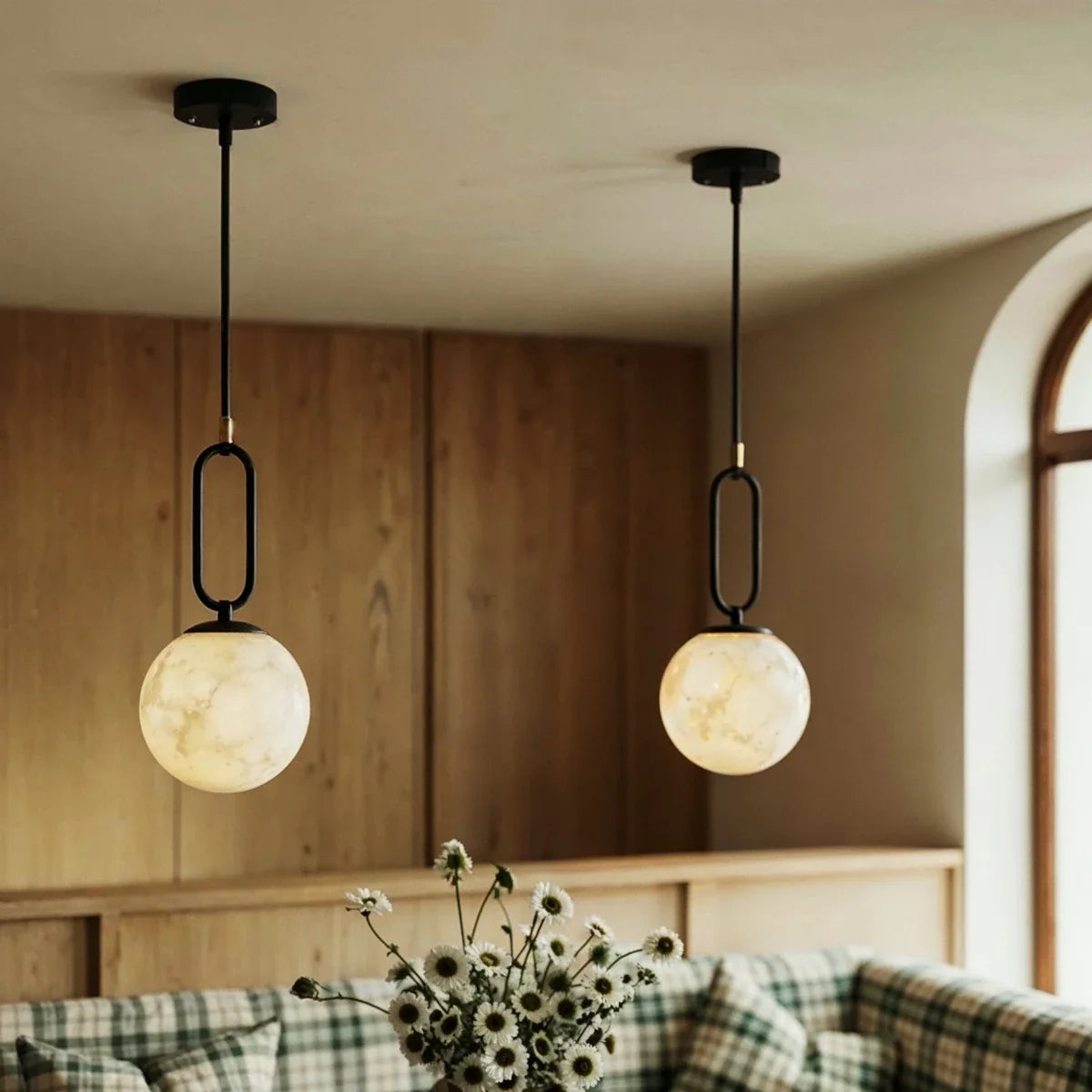 Clérachic pendant lights with black oval hardware and alabaster globes, glowing above a plaid dining banquette.