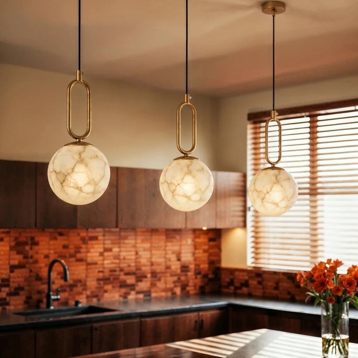 Clérachic gold pendant lights with alabaster globes, three glowing above a dark wood kitchen island and sink.